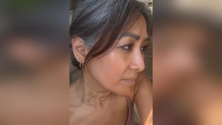 Close-up of a woman with natural gray hair looking to the side, reflecting confidence and beauty in midlife.