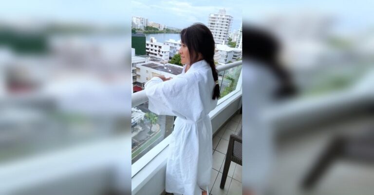 Woman in a white robe standing on a hotel balcony in Puerto Rico, beginning her gray hair journey after her last dye in October 2024.