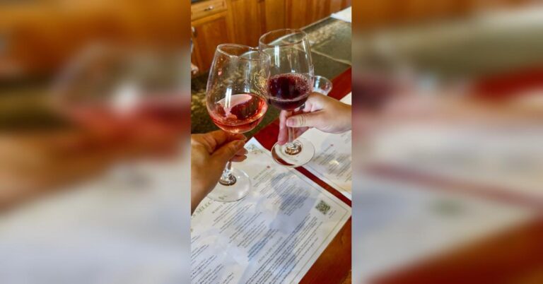 Two hands clinking wine glasses—one rosé, one red—during a tasting at South Coast Winery in Temecula, with tasting menus in the background.