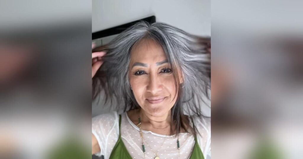 Meesh holding up her hair to reveal the natural gray grow-out at nine months, showing the contrast and progress of her transition with confidence.