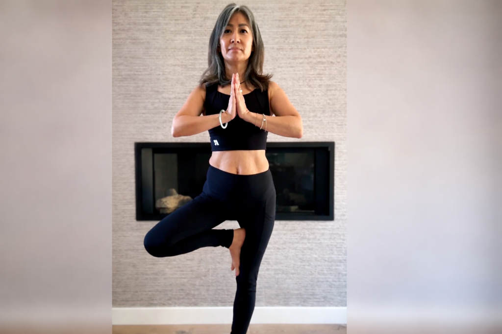 Woman practicing yoga balance pose at home, reflecting strength, awareness, and listening to the body