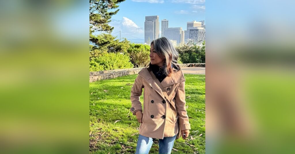 Woman with natural gray hair standing in a quiet San Francisco park, taking in the city skyline on a clear afternoon.